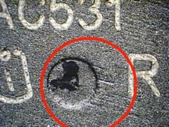 A grey part is visible with white letter markings. A red circle draws attention to an indent with directional sanding marks.