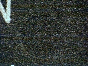 Counterfeit example showing a black textured surface with an indent that has an uneven filling with blacktopping