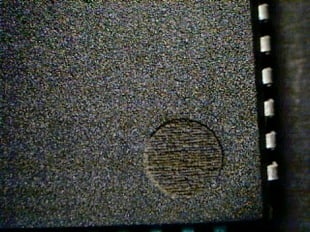 A dark grey counterfeit part is showing with what a circle that looks a bit like an indent but is not