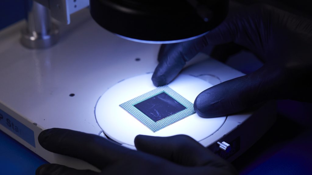 Gloved technician inspecting an electronic component under a microscope in AERI's in-house test lab